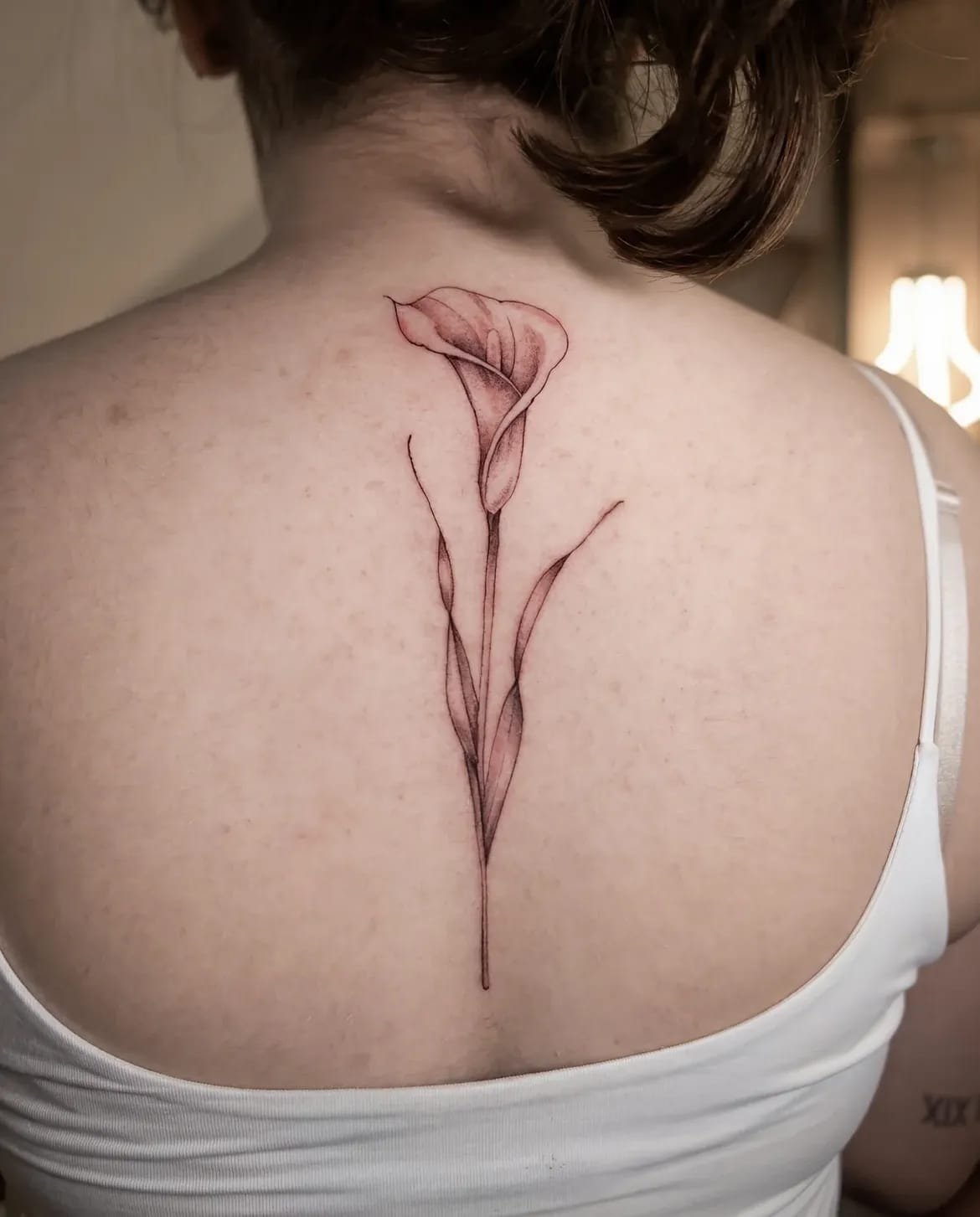 Single fine-line calla lily tattooed along a client’s spine.